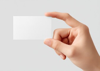 A hand holding a blank rectangular card against a soft grey background