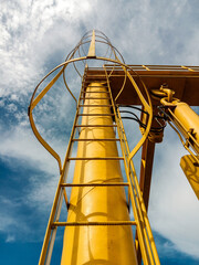 Low angle view of a yellow industrial metal ladder with safety cage against blue sky. © L'Graph