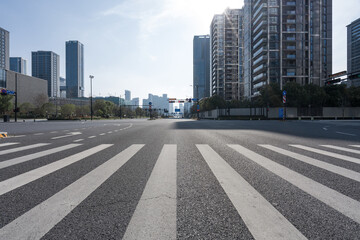 Empty urban street with zebra crossing and modern high-rise buildings under clear morning light © zhu difeng