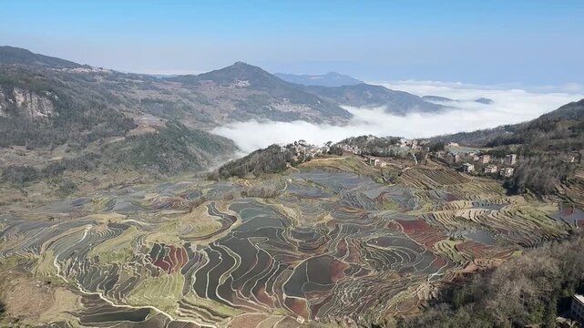 Epic time-lapse of a sea of clouds flowing over the UNESCO World Heritage Hani Rice Terraces in Yunnan, China. Water-filled terraces reflect the sky amidst a mystical mist.