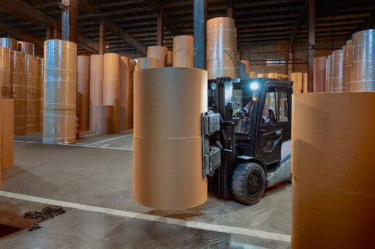 Forklift moving large paper rolls in a spacious warehouse at a paper mill during nighttime operations