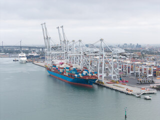 Overhead View of a Bustling Port of Melbourne Container Terminal with Ships, Gantry Cranes, and City Skyline
