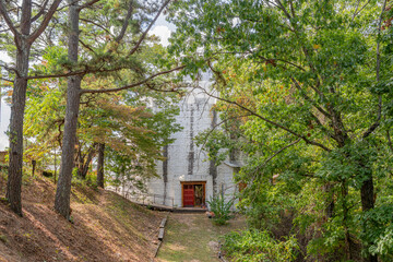 Naklejka premium White stone house with red door nestled among tall trees.