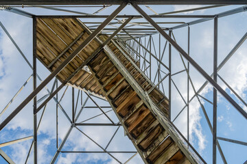 Fototapeta premium Metal tower staircase ascends toward blue sky with clouds.