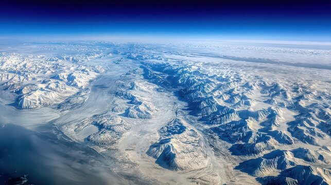 Aerial View of Snow Capped Mountain Range Under Clear Blue Sky With Peaks Valley Ridges Ice and Snow From High Altitude Perspective During Daytime