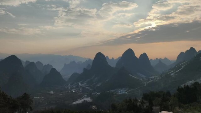 An epic time-lapse capturing thick clouds moving rapidly over the majestic karst mountain peaks in Yangshuo, Guilin. The soft morning light illuminates the valley and traditional villages in Guangxi, 