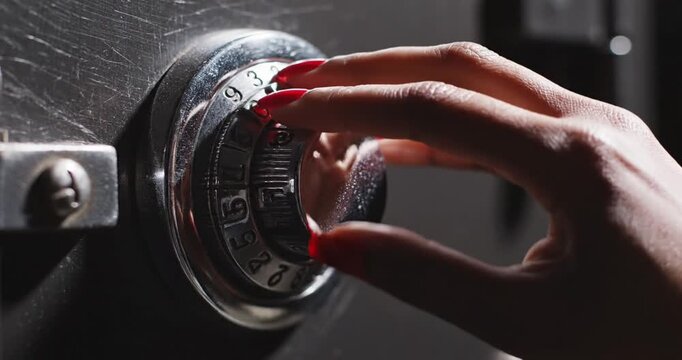 Close-up of a hand with red nails turning a combination lock on a secure safe in a dimly lit room