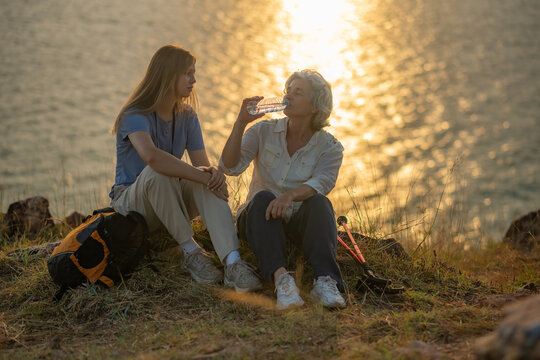 hikers resting and sharing a drink while sitting on a coastal cliff at sunset enjoying a peaceful break during their outdoor adventure backpacks and hiking gear.