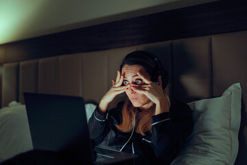 Woman Covers Her Eyes But Can Not Stop Looking at Laptop. Curious woman peeking through her fingers...