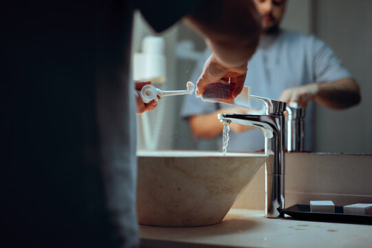 Man Puts Toothpaste on Toothbrush in Bathroom Before Bedtime. Close-up of a man applying mint paste to a brush for his nightly dental care 