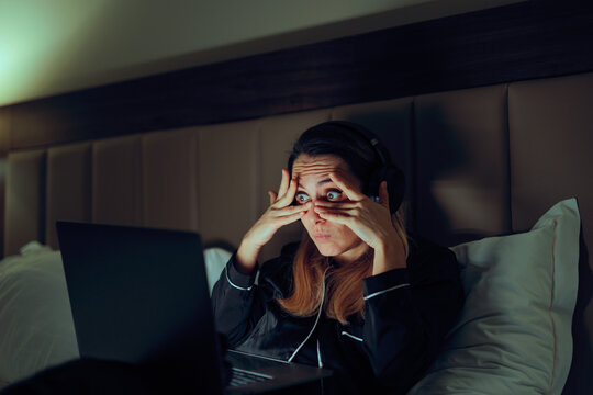 Woman Covers Her Eyes But Can Not Stop Looking at Laptop. Curious woman peeking through her fingers at a laptop screen feeling shame 