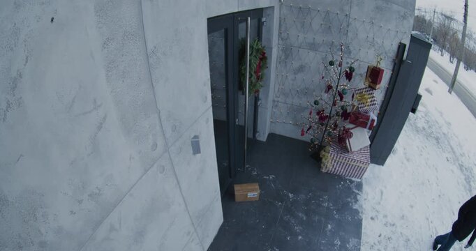 Female Passerby Approaches Festively Decorated House, Notices Parcel on Porch, Quickly Picks It Up, And Walks Away. Camera Captures Package Theft During Christmas Season. Concept of Safety Concerns.