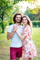 Happy couple standing close together in a sunny park, smiling and holding hands