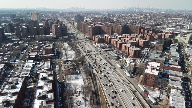 Urban aerial perspective of the bustling cross bronx expressway during winter, showcasing heavy traffic with the iconic manhattan skyline visible in the distant background on a sunny day