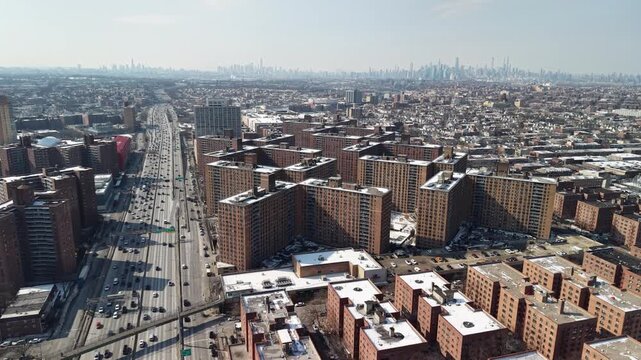 High altitude drone footage capturing highway traffic in queens, with numerous brick apartment buildings under a layer of snow and the distant manhattan skyline visible on the horizon