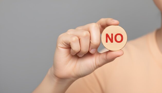 A person's hand holds a round wooden token with the word 'NO' written in red, symbolizing refusal or denial.