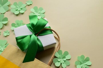 St. Patrick's day gift box. Paper bag with gift box among clover leaves on beige background