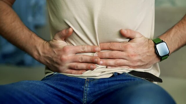 Man Clutching His Stomach with Both Hands Due to Severe Abdominal Pain. Experiencing Gastritis Symptoms or Food Poisoning
