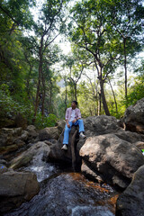 Obraz premium Young man relax on rock amidst forest stream, serene nature escape
