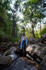 Obraz premium Young man relax on rock in lush green forest near flowing river stream