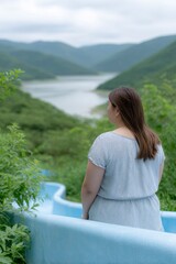 An woman climbing up the side of an empty blue water slide, facing away from the camera with her back to the viewer, overlooking green mountains and a lake