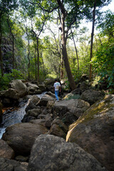 Man Navigates Rocky Terrain Near Stream, Lush Forest Surroundings