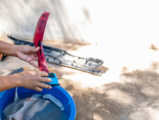 Hands of a worker wet sanding plastic car parts with waterproof sandpaper in a blue basin.