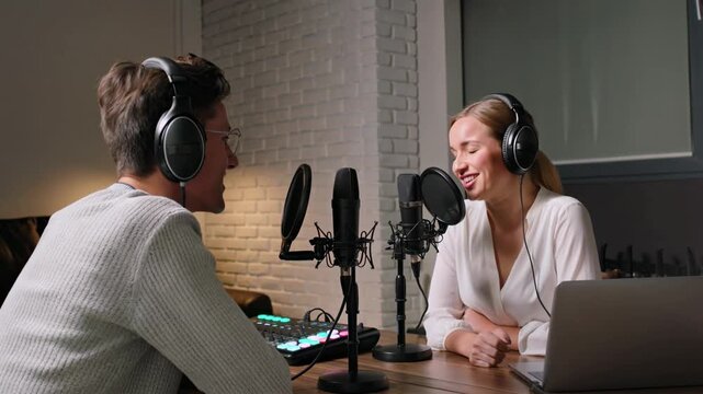Two people engaged in a lively podcast recording session, smiling and interacting with microphones and headphones in a studio setting