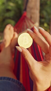 Vertical video. First Person Perspective Holding Golden Bitcoin Coin Above Hammock in Tropical Forest With Warm Light Showing Digital Gold and Long Term Wealth Vision