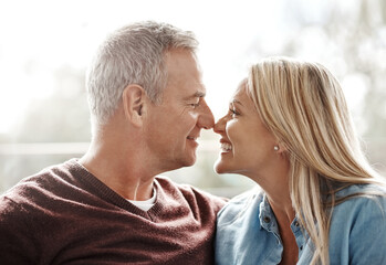 Fototapeta premium Love, nose touch and happy with couple on sofa for marriage, bonding or support together. Smile, relax and connection with mature man and woman in living room of home for loyalty, commitment and care