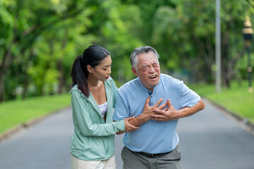 Obraz premium Elderly man suffering from chest pain and heart attack during outdoors exercise with young woman assisting. Senior Asian male having sudden stroke symptom while jogging in park with lady helping.