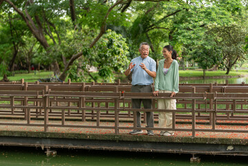 Smiling senior man and young woman having romance love conversation dating outdoors in greenery nature. Happiness age gap couple enjoying date relationship and talking together in public park.
