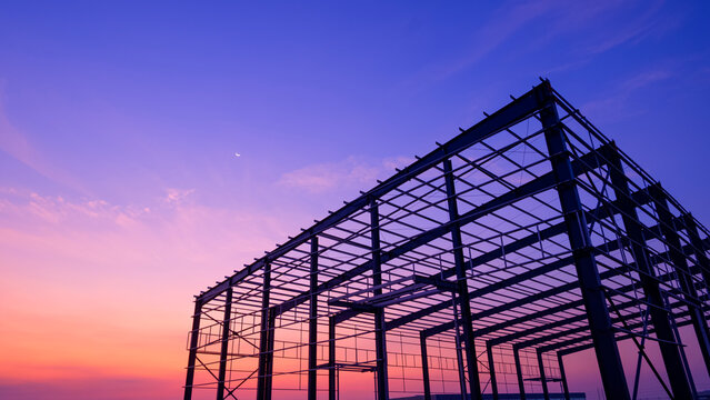 Silhouette steel structure of industry warehouse factory building with metal framework in construction site against colorful twilight sky background, low angle view with copy space