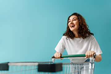 Cheerful Woman Shopping with Cart on Vibrant Blue Background