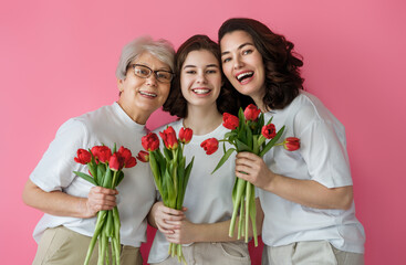 Three Generations of Women Smiling with Red Tulips Against Pink Background