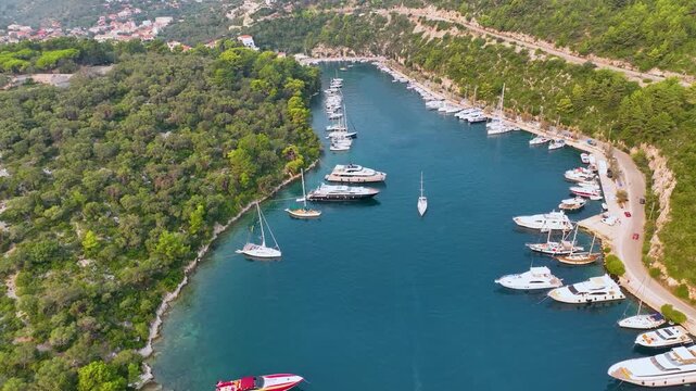 Aerial View of Luxury Yachts and Sailboats Anchored in the Scenic Narrow Channel of Gaios Port on Paxos Island Greece Surrounded by Lush Green Pine Trees and Turquoise Ionian Sea