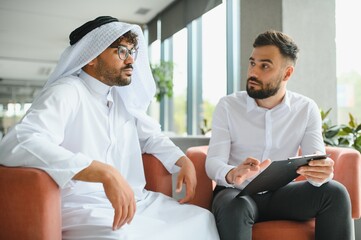 Obraz premium International operations manager discussing business with saudi partner in traditional kandura