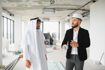 Architect showing construction plans to arab investor in building under construction
