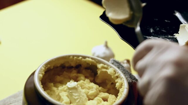 Person adds butter to mashed potatoes to enrich the flavor and texture