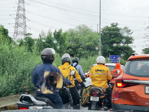 Delivery rider from indian startup offering 10 min delivery in quick commerce hyperlocal Blinkit stuck in traffic in rain showing the challenges faced by gig economy workers