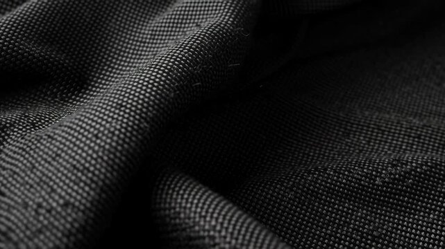 A close up of a black fabric with a pattern. The fabric is wrinkled and has a rough texture. the surface of dark textured fabric, revealing fine woven patterns and soft folds in dramatic light 