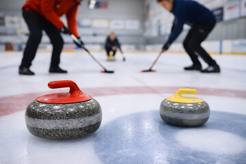 Curling Stones on Ice with Players Sweeping in Indoor Rink
