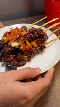 Close up of a female hand holding a plate of beef satai Indonesian food