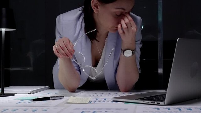 Stressed business woman suffering from headache in dark office, hands on head experiencing burnout and fatigue during late night work, facing deadline pressure and financial difficulties