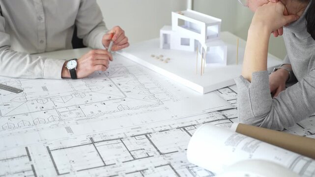 Architects engaging in a design planning meeting, analyzing blueprints and a scale model, making precise measurements and discussing new construction project ideas, close up