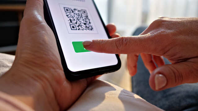 A hand holds a smartphone displaying a QR code, ready to scan for contactless payment. The scene suggests online shopping or digital banking, emphasizing convenience and modern financial transactions.