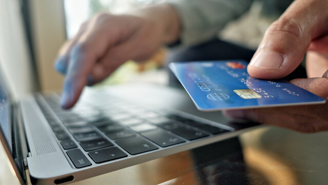 A person's hands hold a blue credit card over a laptop keyboard, indicating an online transaction. The setting highlights digital payments, online shopping, and financial transactions.