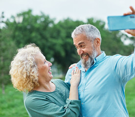Happy active mid aged couple taking selfie in park or in nature outdoors. Love togetherness and acive seniors vitality concept