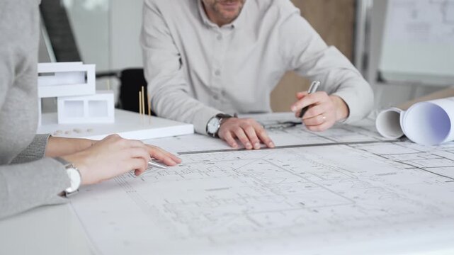 Architects are teamwork planning a building design project, reviewing detailed blueprints with a compass and a ruler, working on technical drawings and a digital tablet at the office, close up