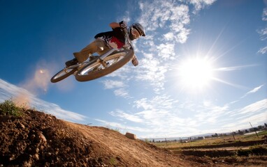 Fototapeta premium BMX Rider Launching Off Dirt Jump Under Bright Sky